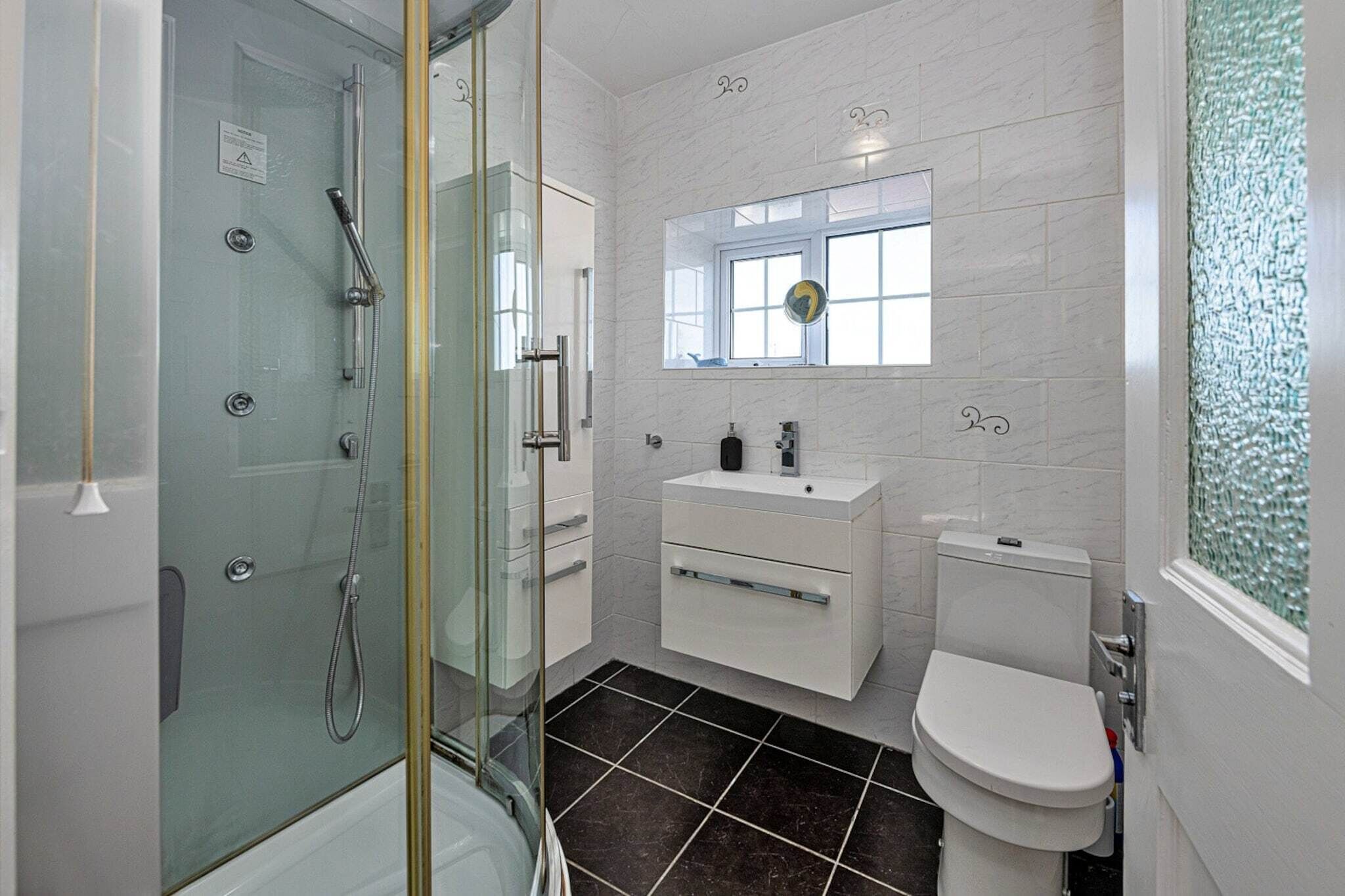 A modern bathroom with a glass-enclosed shower, a white sink with a mirror above it, and a toilet.