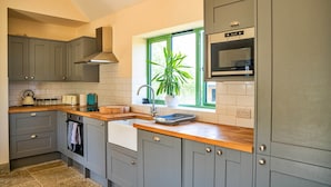 A kitchen with grey cabinets, a wooden countertop, a built-in oven, and a window with a plant. - Annexe in Cotswolds near Bourton-on-the-Water (Little Rissington)