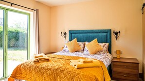 A bedroom with a large bed, two bedside tables, a window with curtains, and a view of greenery outside. - Annexe in Cotswolds near Bourton-on-the-Water (Little Rissington)