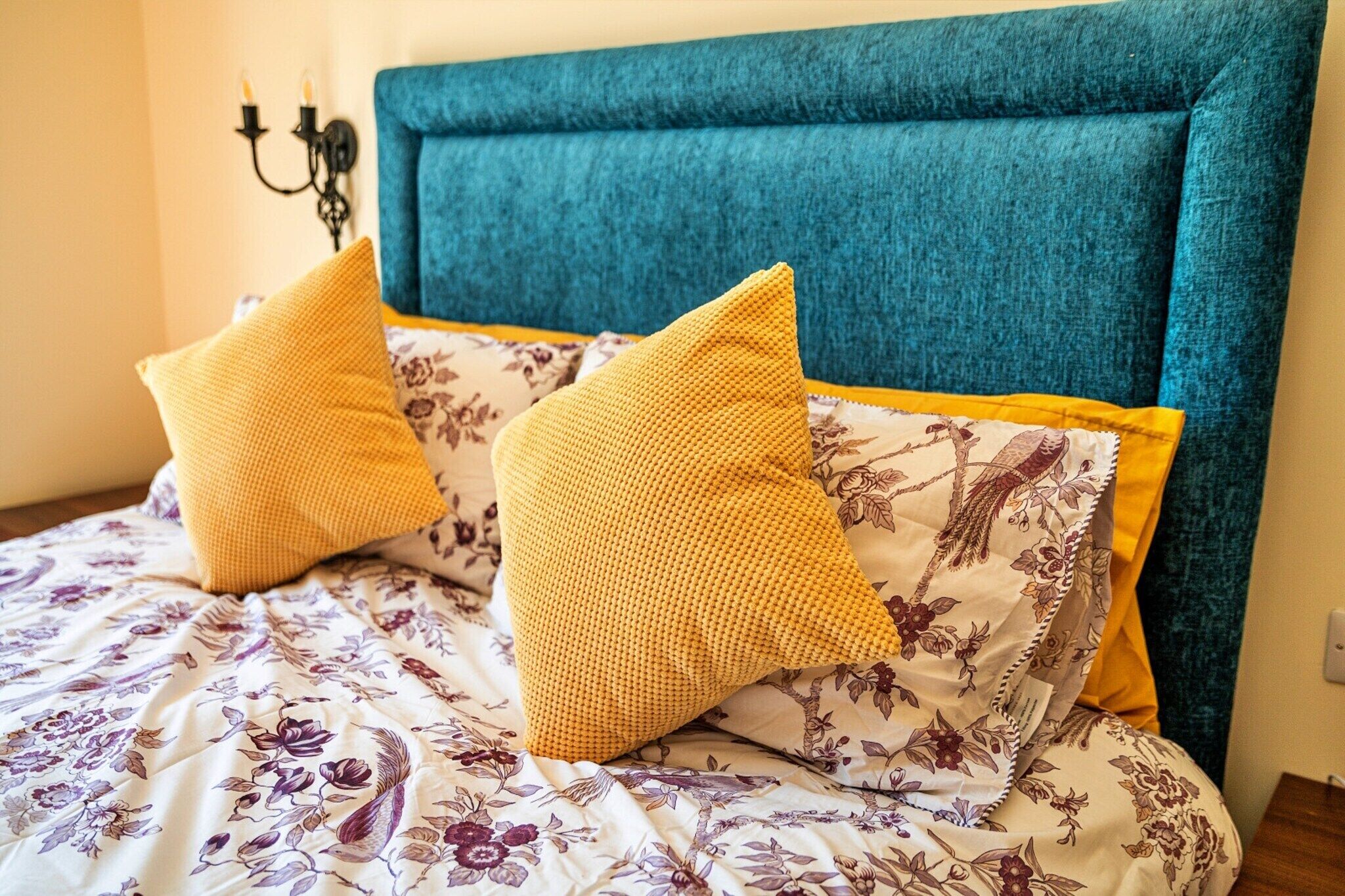 Una cama con una colcha de estampado floral y dos almohadas amarillas.
