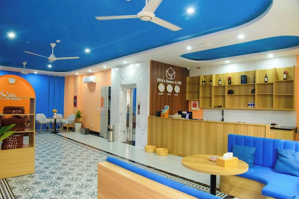A hotel reception area with a blue and orange color scheme, a reception desk, seating area, and ceiling fans. - Tina's House & Spa (Phu Quoc)