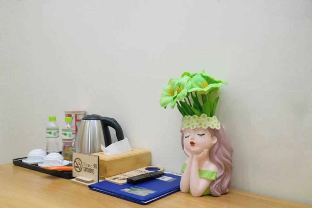 Een bureau met een bordje 'ROKEN VERBODEN', een waterfles, een thermoskan, een pak zakdoekjes, een afstandsbediening en een decoratief beeldje met een boeket groene bloemen.