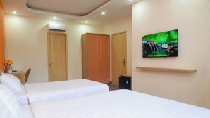 A hotel room with two beds, a TV on the wall, and a small desk with a vase of flowers. - Tina's House & Spa (Phu Quoc)