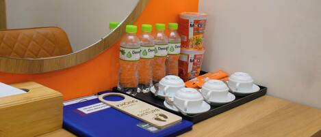 A hotel room with a wooden desk, a blue folder, a wooden footrest, and a tray with cups and bottles.
