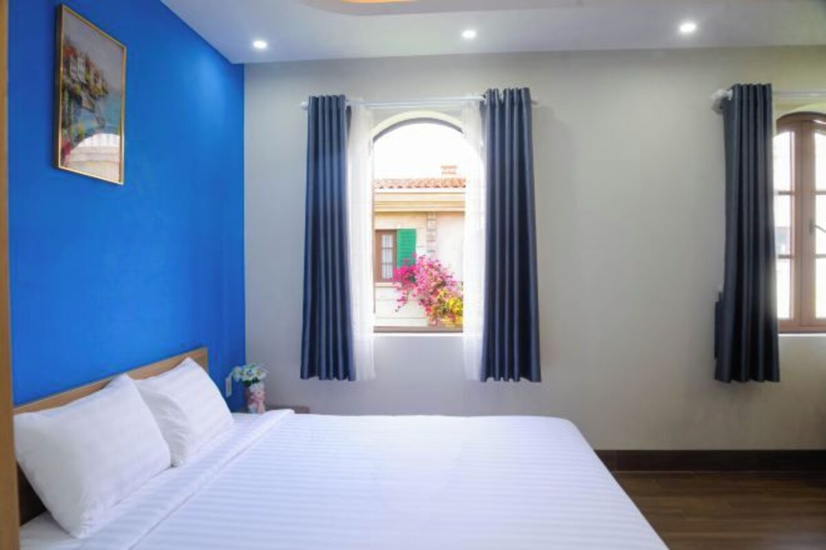 Hotelkamer met een groot bed, een raam met gordijnen, uitzicht naar buiten en een schilderij aan de muur.