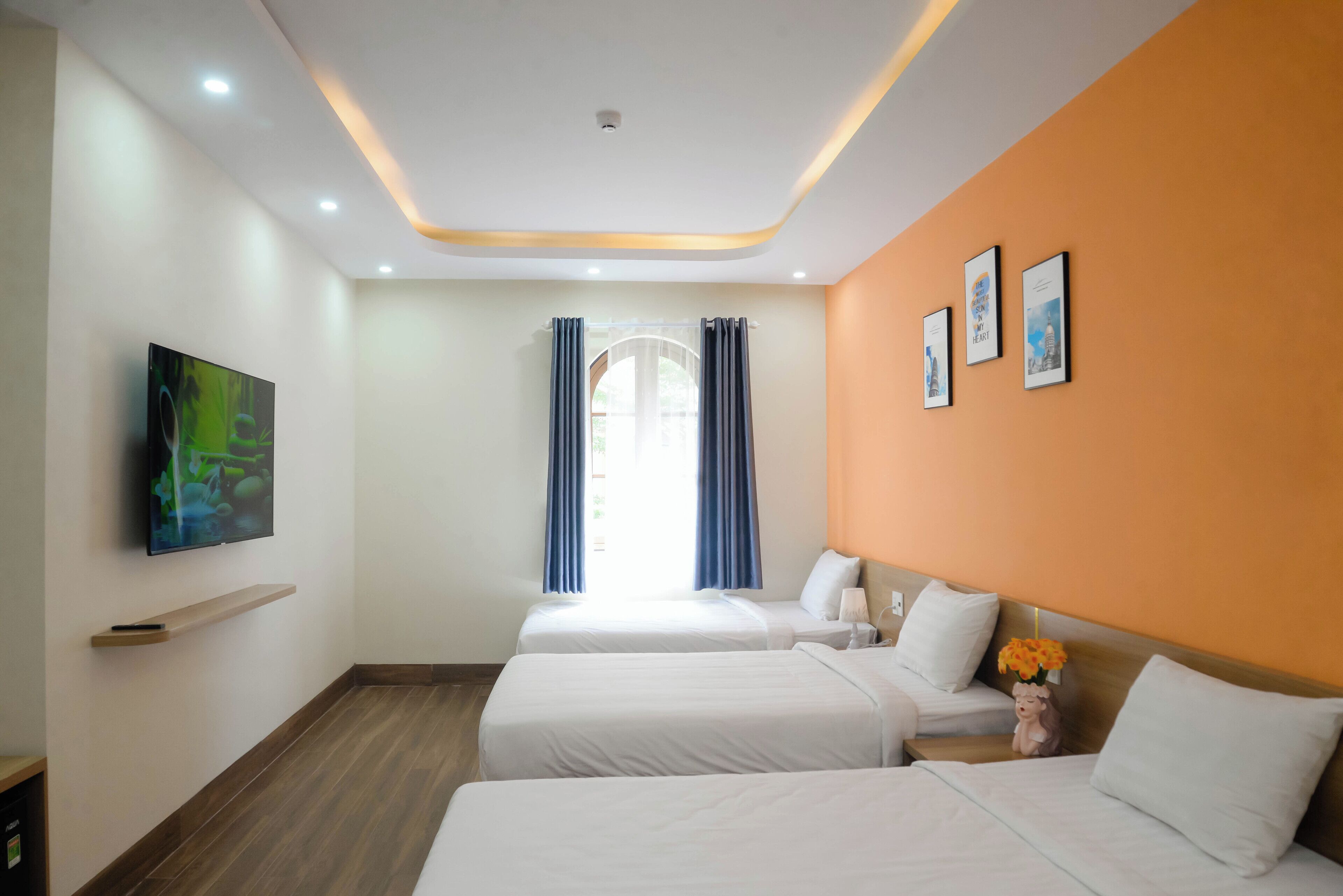 A hotel room with two beds, a TV, a shelf, and a window with curtains.