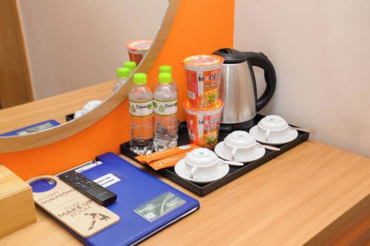 Hotelkamer met een spiegel, een dienblad met een koffiezetapparaat, waterflessen, een dienblad met kopjes en een afstandsbediening, een make-up tas en een blauwe map.