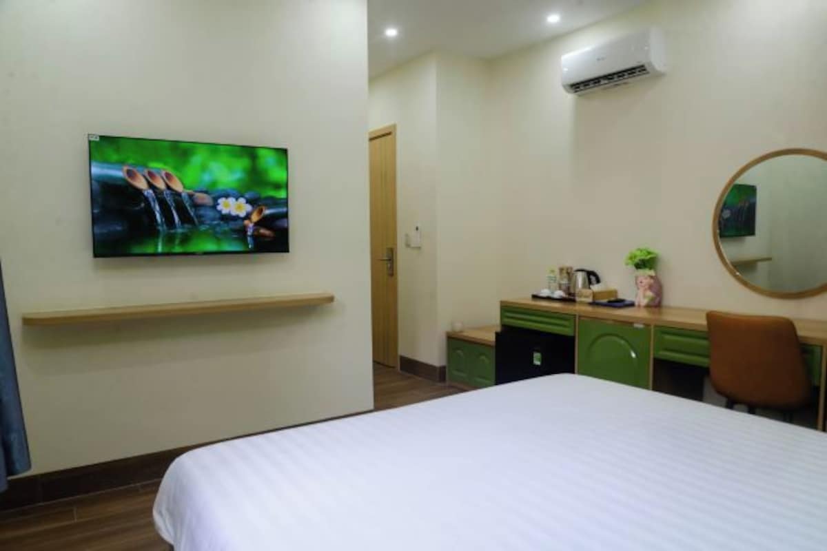 A hotel room with a bed, a desk, a chair, a television mounted on the wall, and a mirror.