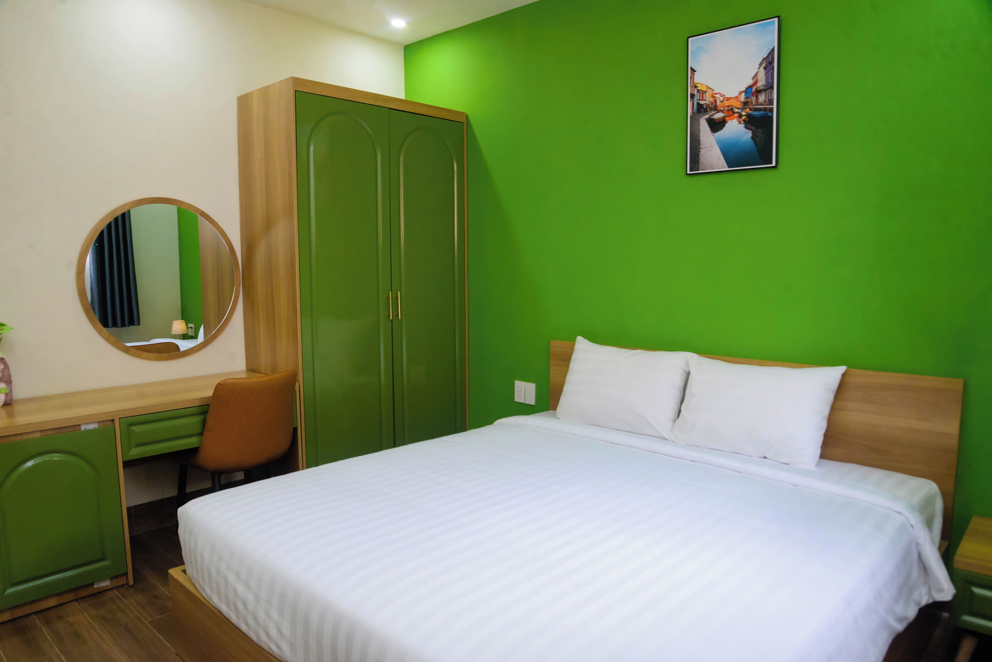 A hotel room with a bed, a desk, a chair, a wardrobe, and a mirror.