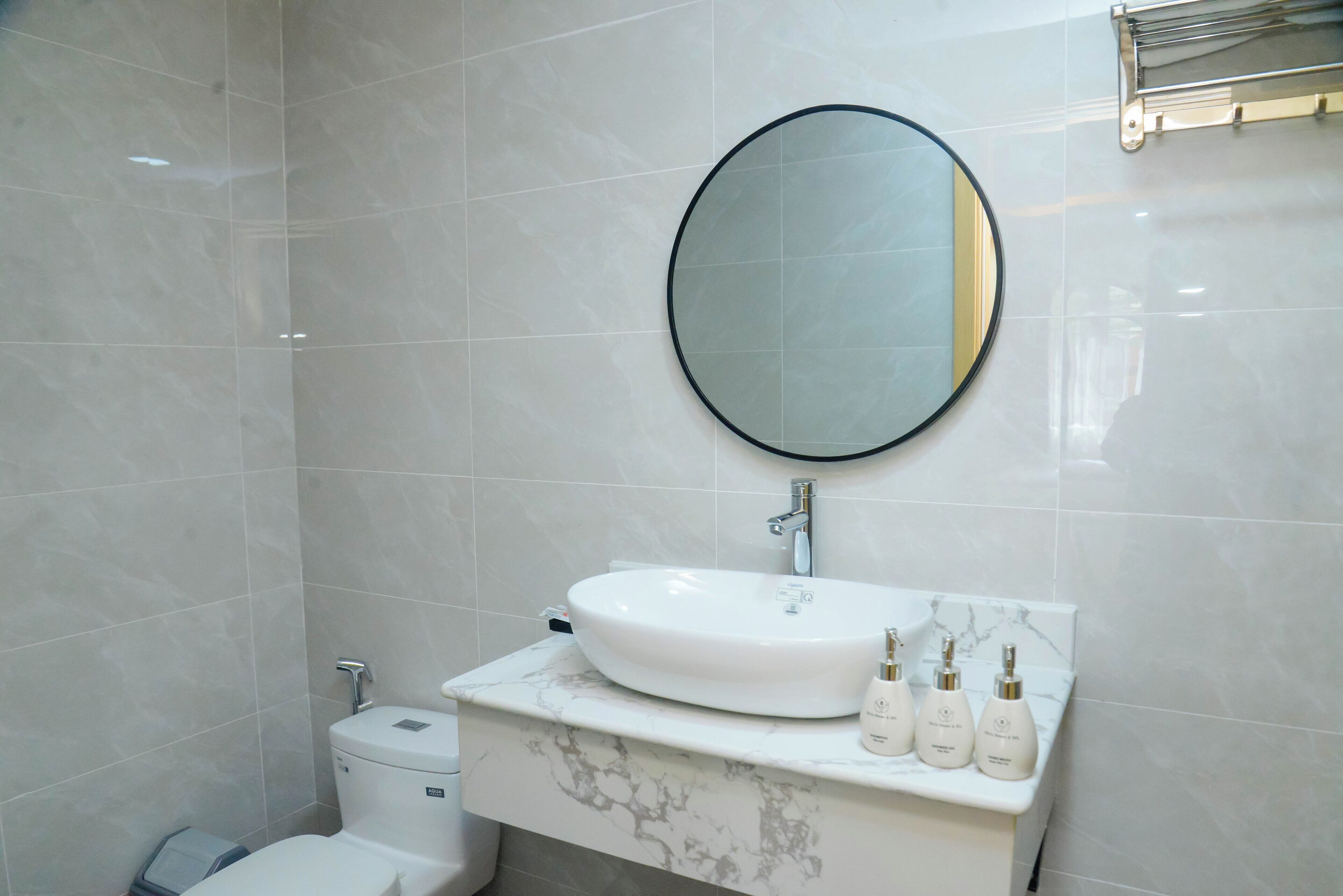 A bathroom with a white marble sink, a round mirror, and three toiletries on the counter.