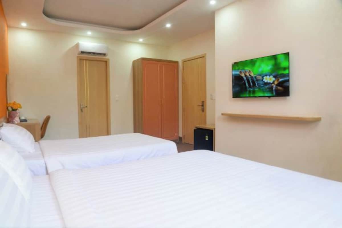 A hotel room with two beds, a TV on the wall, and a small desk with a chair.
