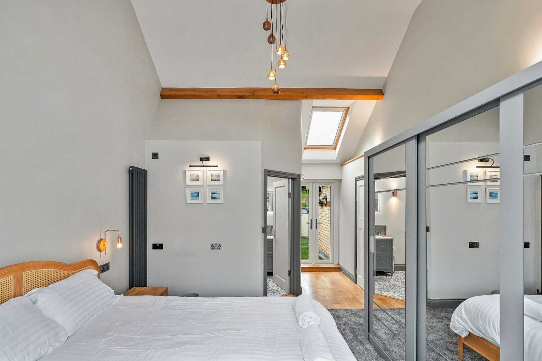 A modern hotel room with a large bed, a skylight, and a sliding glass door leading to a balcony.
