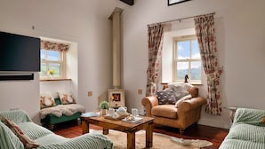 A cozy living room with a fireplace, green sofas, a wooden coffee table, and floral curtains. - Beautiful holiday cottage in Chittlehampton, No deposit (Llandrillo)