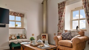 A cozy living room with a sofa, a chair, a table with a tray of tea and cookies, a fireplace, and a window with curtains. - Beautiful holiday cottage in Chittlehampton, No deposit (Llandrillo)
