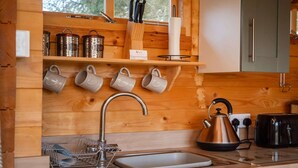 Een keuken met houten kastjes, een roestvrijstalen spoelbak, een waterkoker en een broodrooster.