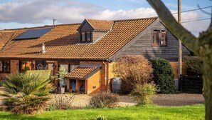 A rustic house with a sloped roof, a small attached garage, and a solar panel on the roof. - Cottage in Norfolk near River Yare (Surlingham)