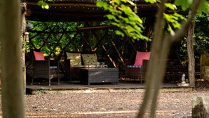 A covered outdoor seating area with wicker furniture and cushions, surrounded by trees and a wooden deck. - Cottage for 6 guests in Woolton Hill. (Woolton Hill)