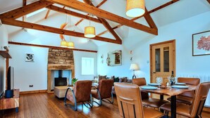A spacious living area with a stone fireplace, wooden beams, and a dining table set for four.