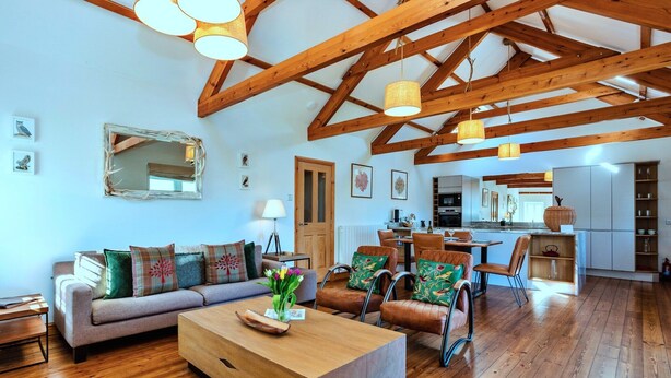 A spacious living room with wooden beams, a sofa, chairs, and a coffee table.