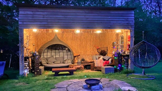 A cozy outdoor seating area with a cushioned bench, a hanging chair, and a fire pit. - Shepherd's Hut in Romsey with Fire Pit (Romsey)