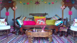 A cozy room with a wooden sofa adorned with colorful cushions, a patterned rug, and a decorative star hanging from the ceiling. - Shepherd's Hut in Romsey with Fire Pit (Romsey)