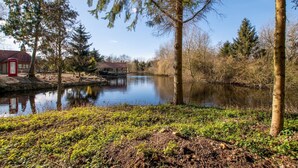 A riverside scene with a traditional red telephone booth, a wooden bridge, and a building with a red roof. - Cottage on Private Island in Cambridgeshire (Ramsey)