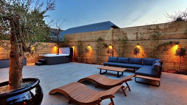 An outdoor patio with wooden loungers, a sofa, and a hot tub. - Holiday Home in Kent with Hot Tub & Games Room (Appledore)