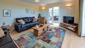 A living room with a leather sofa, wooden coffee table, and a TV stand. - Bungalow in Dyserth with Hot Tub & Waterfall (Dyserth)