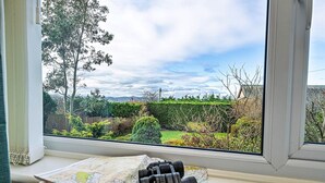 A window with a map and binoculars on a windowsill, overlooking a garden with trees and a hedge. - Bungalow in Dyserth with Hot Tub & Waterfall (Dyserth)