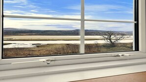 A window with a view of a landscape including a river, trees, and distant hills. - Cottage by Loch with Stunning Views (Achahoish)