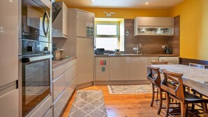 Una cocina compacta con electrodomésticos modernos, una zona de comedor con sillas de madera y un ventanal que proporciona luz natural.