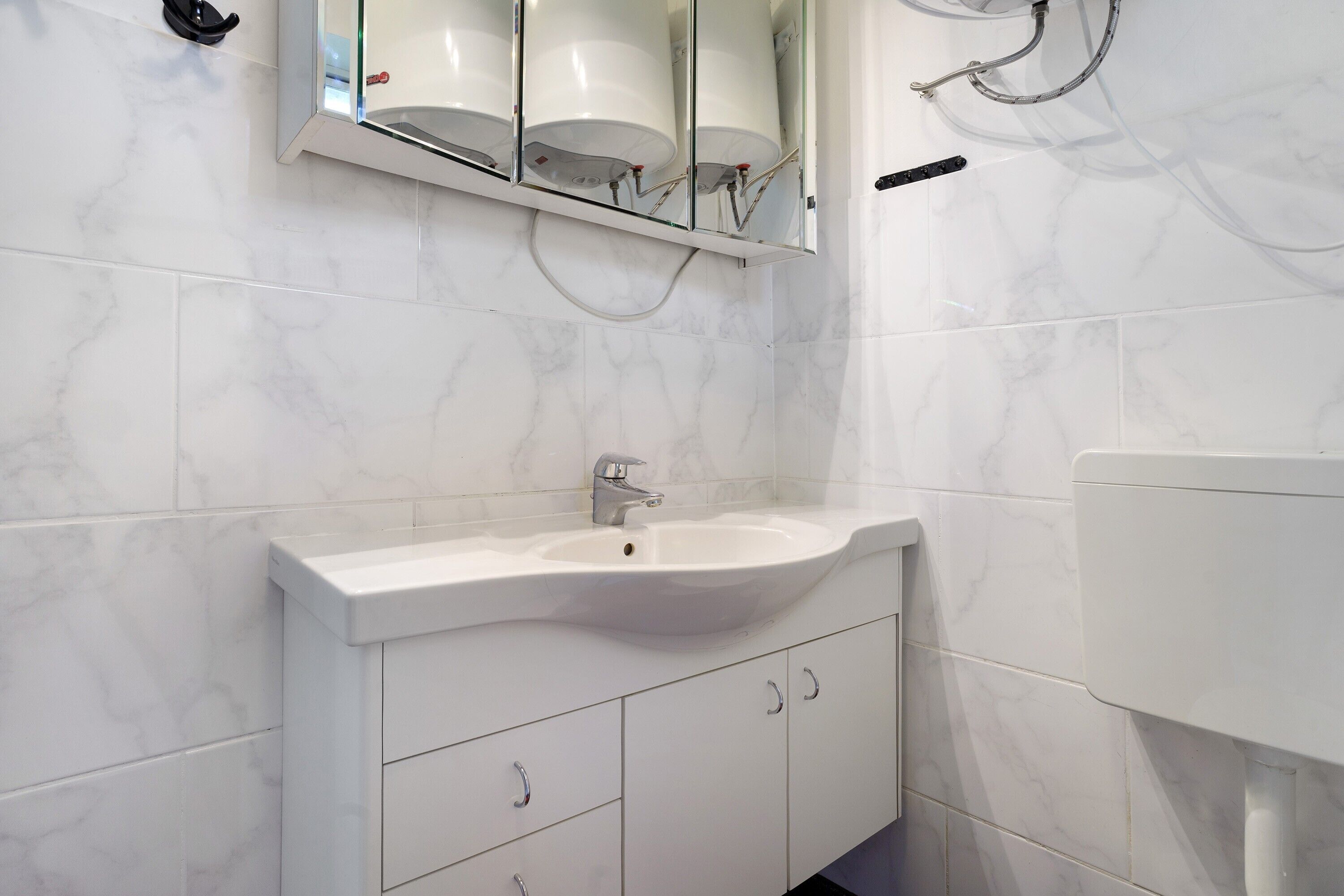 A bathroom with a white sink, a mirror, and marble tiles.