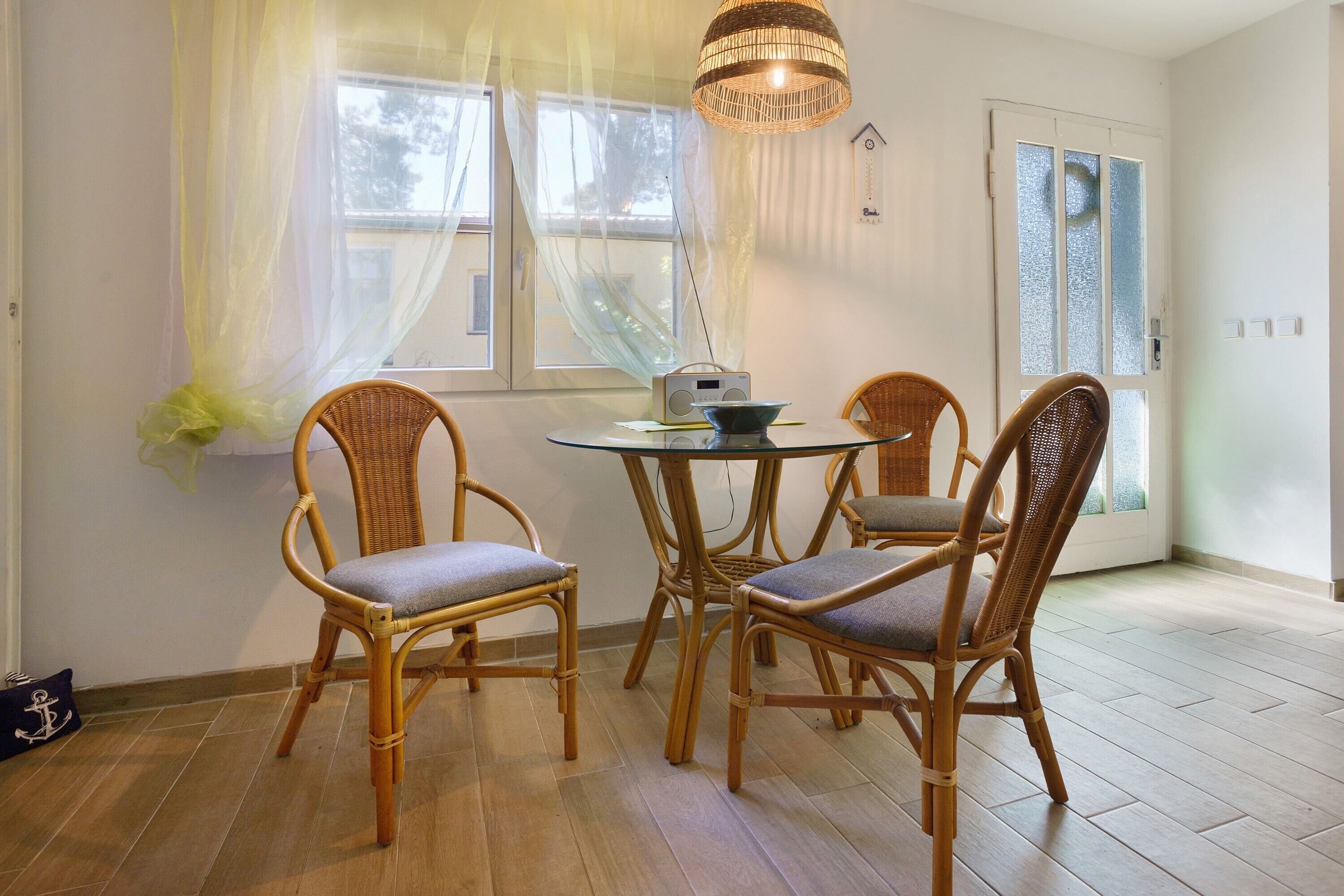 Un coin repas avec des chaises en osier, une table ronde en verre et une radio.