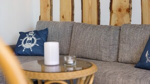 Ein graues Sofa mit einem blauen Kissen, einer weißen Kerze und einem Glaslaternenfuß auf einem runden Holztisch.