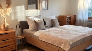 A bedroom with a wooden bed, bedside tables, a small stool, a decorative rug, and wall art.