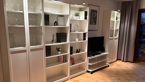 A modern living room with a herringbone wood floor, built-in white shelving units, a flat-screen TV, and a black and white cowhide rug.