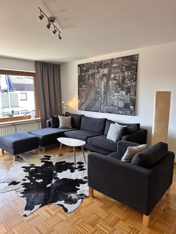 Un salon moderne avec un canapé d’angle, une table basse blanche et un tapis noir et blanc.