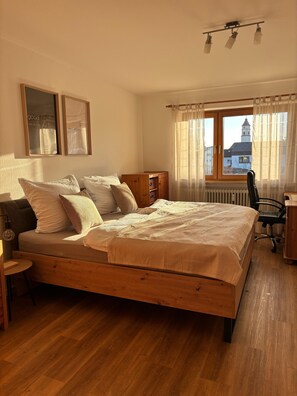 Une chambre à coucher avec un lit en bois, une table de chevet, un bureau, une chaise et une fenêtre avec des rideaux.