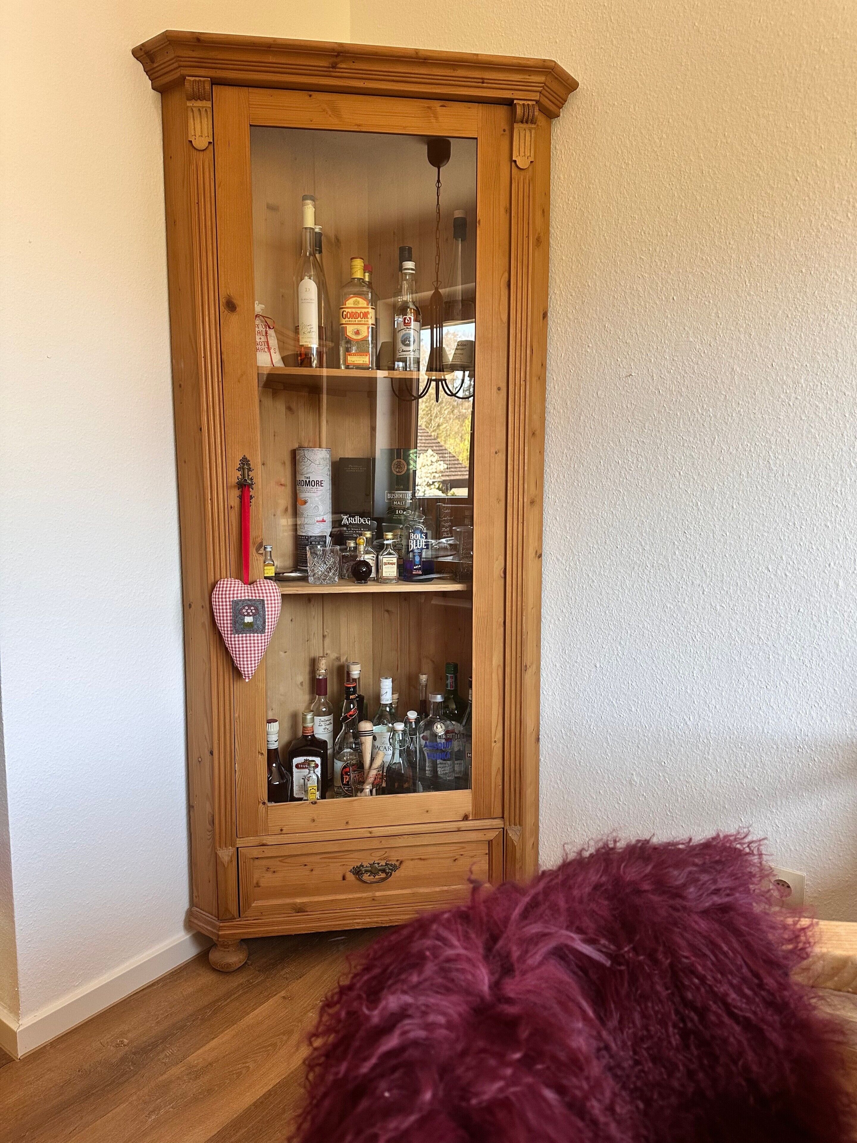 Un meuble en bois doté de portes en verre, contenant diverses bouteilles et boîtes de conserve.