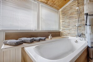 A bathroom with a bathtub, a shower, and a window with blinds.
