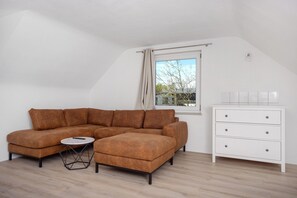 Una habitación con un sofá seccional marrón, una mesita redonda pequeña, un aparador blanco y una ventana con vistas a árboles.