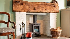 A rustic fireplace with a log shelf, a chair, a basket, and a metal bucket. - Cottage in Carhampton near Dunster Castle (Carhampton)