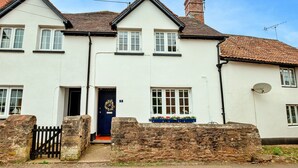 A two-story white house with a dark blue door, a stone wall in front, and a satellite dish on the right side. - Cottage in Carhampton near Dunster Castle (Carhampton)