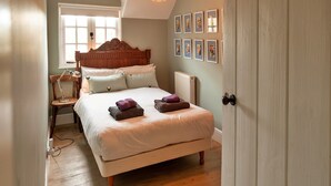 A bedroom with a wooden bed, a nightstand, a chair, and a radiator. - Cottage in Carhampton near Dunster Castle (Carhampton)