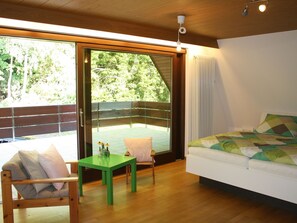 Una habitación con una cama, una mesa verde, una silla y un ventanal corredero que da a un espacio exterior.