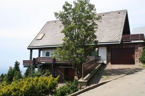 Una casa moderna con techo inclinado, terraza de madera y escalera de piedra.