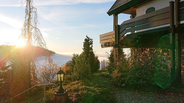 A building with a balcony overlooking a body of water, surrounded by greenery. - Holiday Home 'Talblick' with Mountain View, Private Terrace and Wi-Fi (Sasbachwalden)
