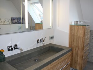 Un baño moderno con un espejo grande, un lavabo de granito, armarios de madera y un mueble de vidrio.