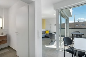 A modern interior with a kitchen, a dining area with a table and chairs, and a living space with a sofa and a lamp.