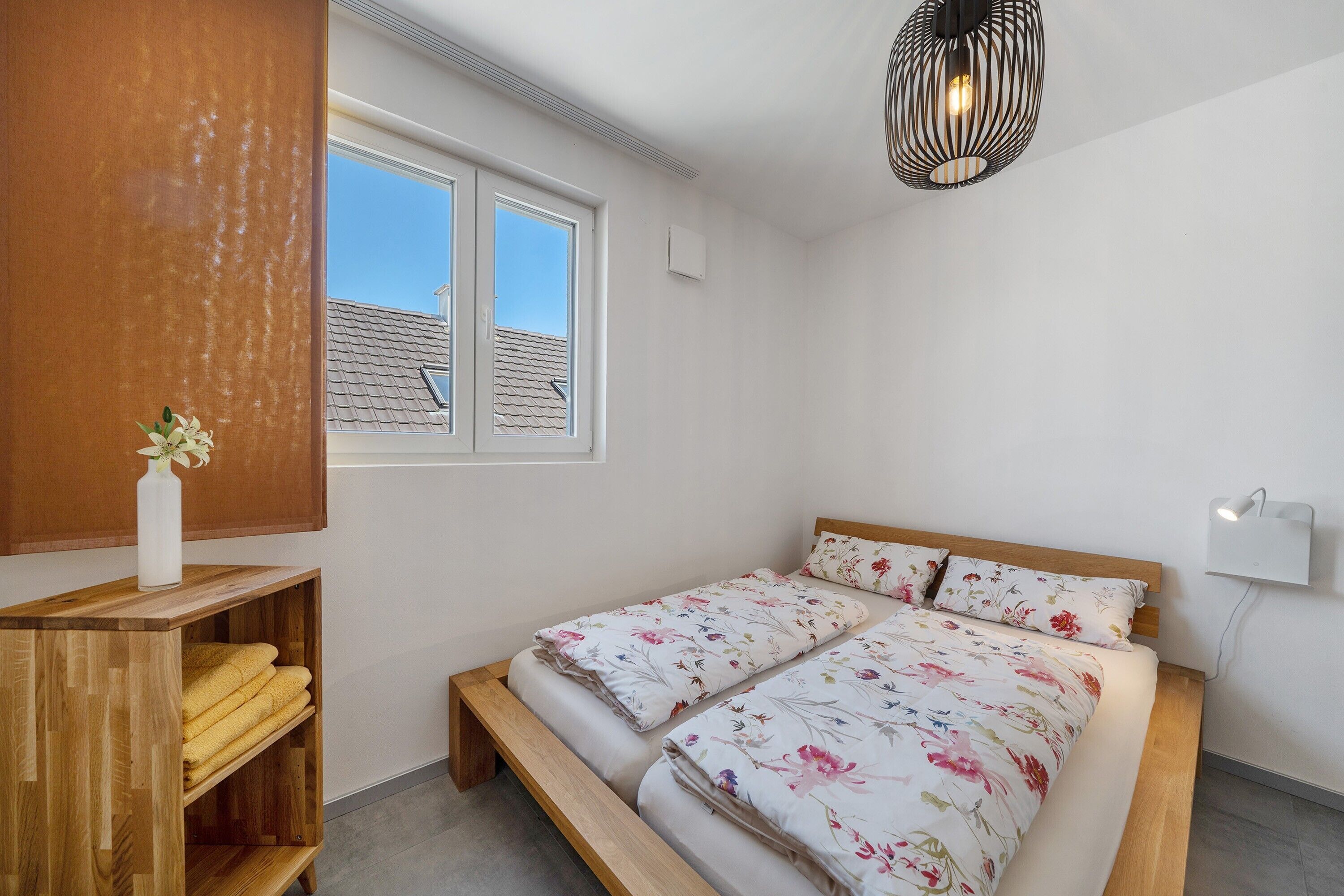Ein Schlafzimmer mit einem Bett, einer hölzernen Bank mit Handtüchern, einem Fenster und einer Wandleuchte.